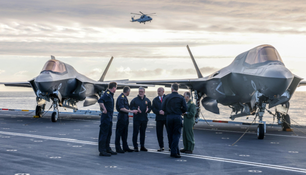 Britain's Prime Minister Keir Starmer (3L) and Britain's Defence Secretary John Healey (3R) stand in front of an Royal Navy F-35B Lightning fighter jet as they talk with Royal Navy Vice Admiral Andrew Burns (L), Commodore James Blackmore, Captain Will Blackett (2R) and Air Wing Commander Captain Colin McGannity (R) on the flight deck of the British aircraft carrier HMS Prince Of Wales, in an undisclosed location, on April 24, 2025, following its deployment to the Indo-Pacific region. (Photo by Richard Pohle / POOL / AFP) (Photo by RICHARD POHLE/POOL/AFP via Getty Images)