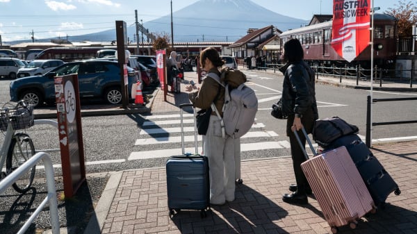 2025年11月22日,游客拖着行李箱,在山梨县富士河口湖町河口湖站外的富士山前行走。
